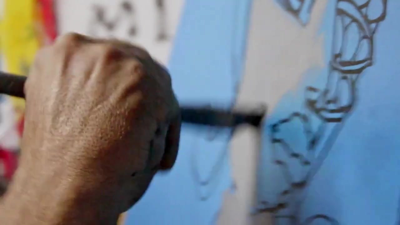 Bazooka Joe's hand drawing a black line across a blue canvas with a marker